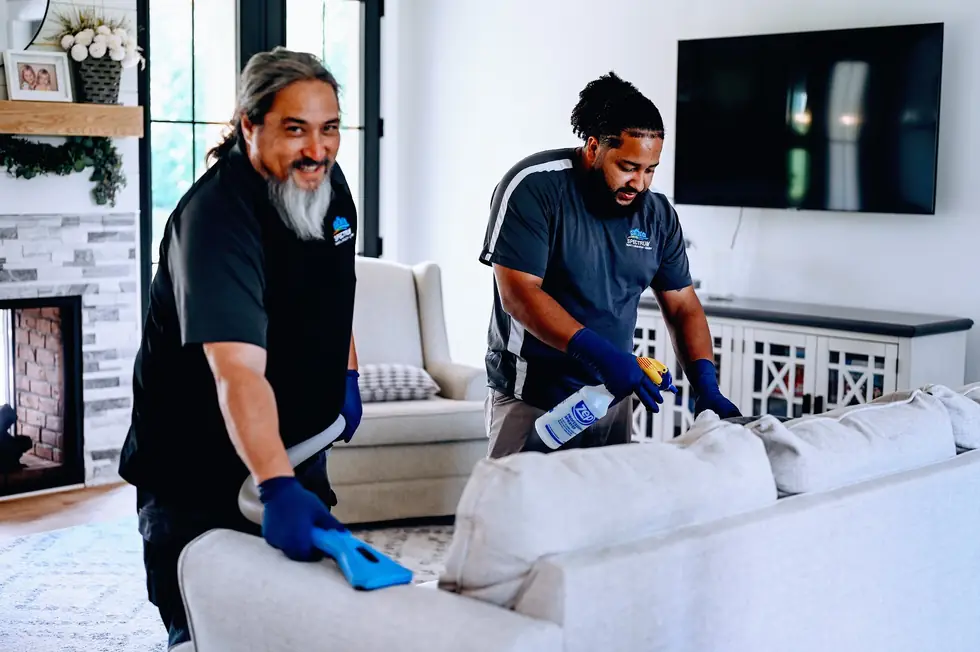 Two Spectrum technicians cleaning a light sofa with an extraction wand and spray bottle