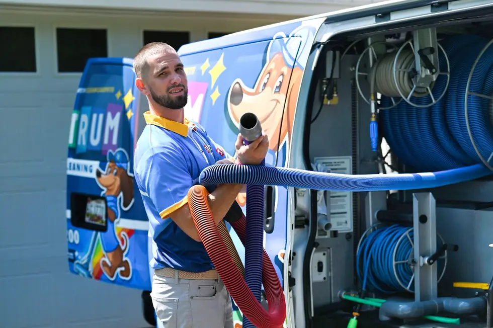 Spectrum technician holding blue truck-mount hoses at the open bay of a van wrapped with the dachshund mascot