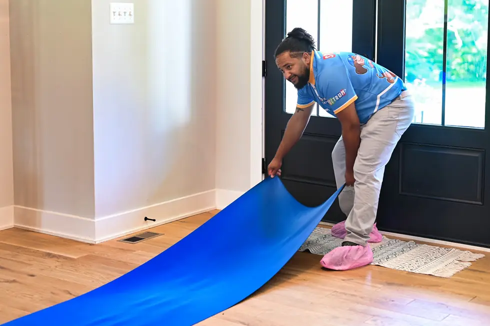 Spectrum technician in shoe covers rolling blue floor protection across a front entry
